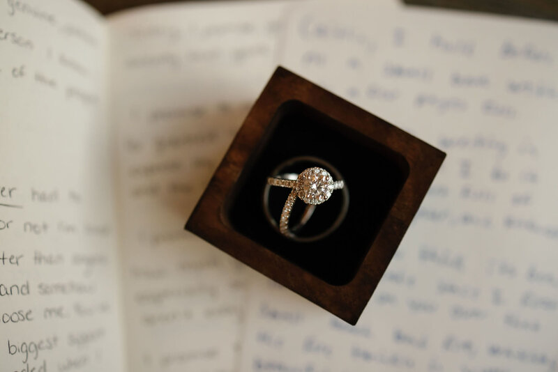 engagement ring and wedding bands in a box sitting on a paper with written vows