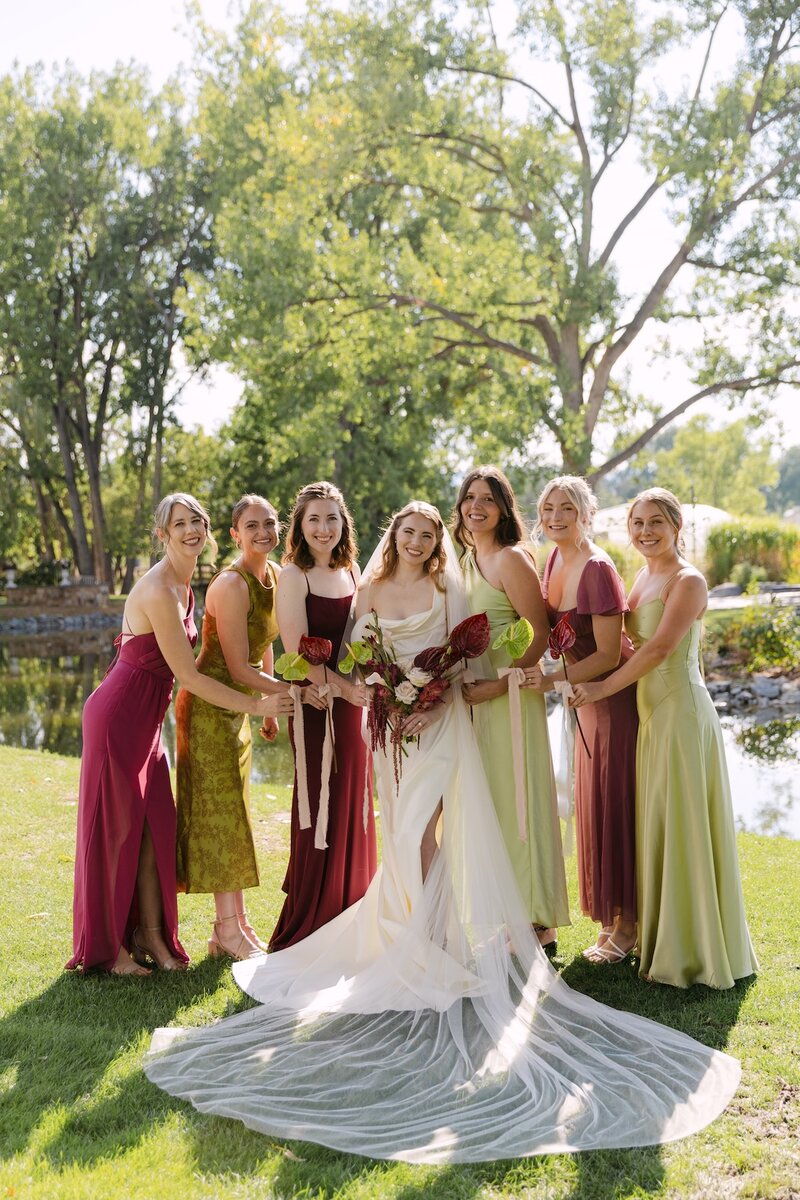 Bride surrounded by bridesmaids in colorful dresses at Hudson Gardens — outdoor Colorado wedding portraits captured by Colorado wedding photographer.