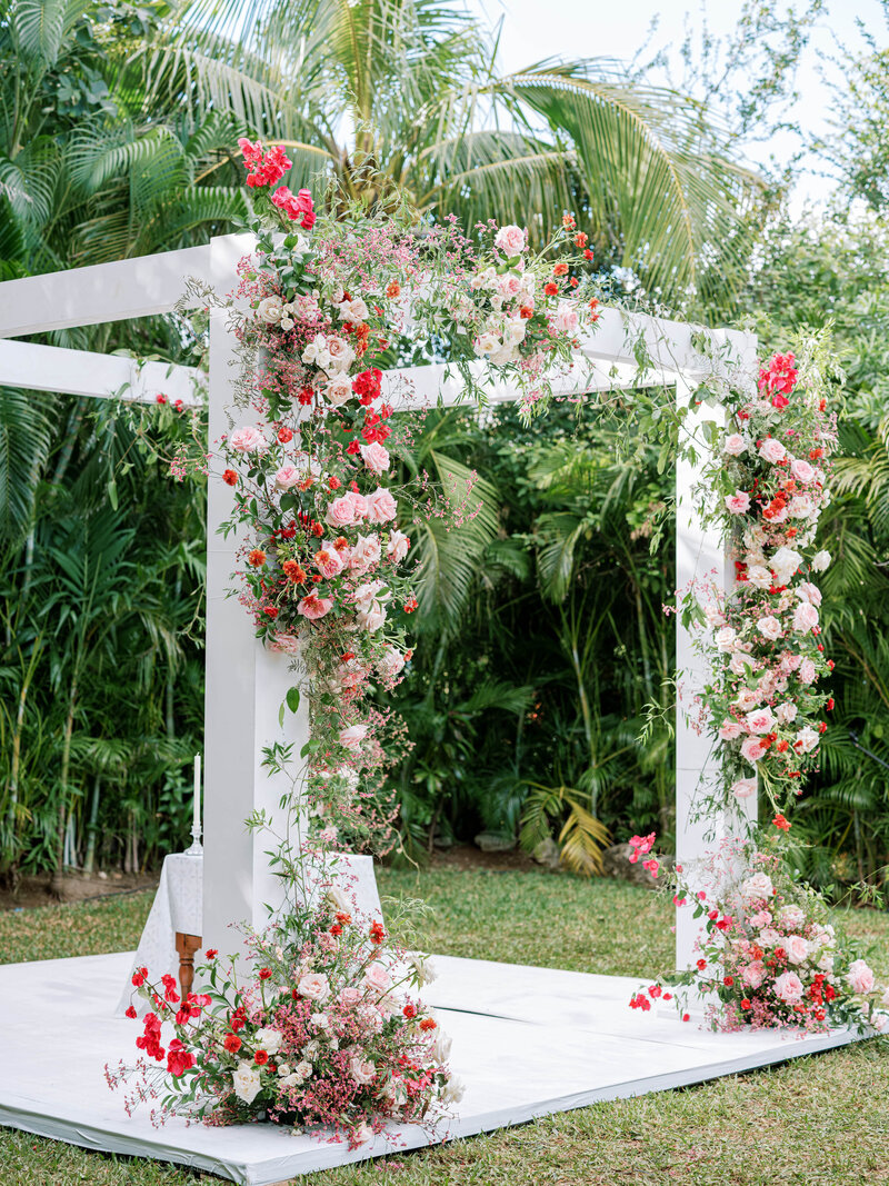 White wood wedding ceremony arbor covered with red and pink flowers