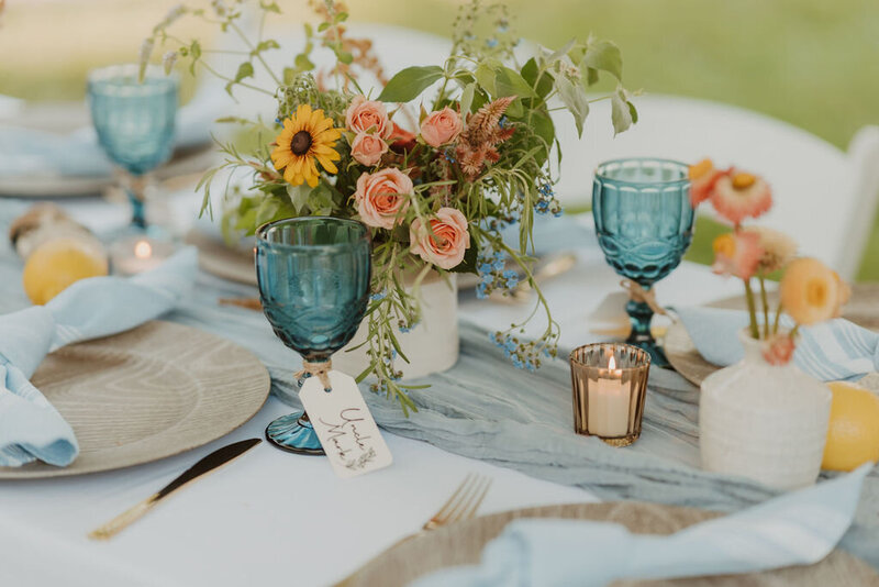 Wedding table display of blue goblets, white candles and florals arrangements of sunflowers and peach roses