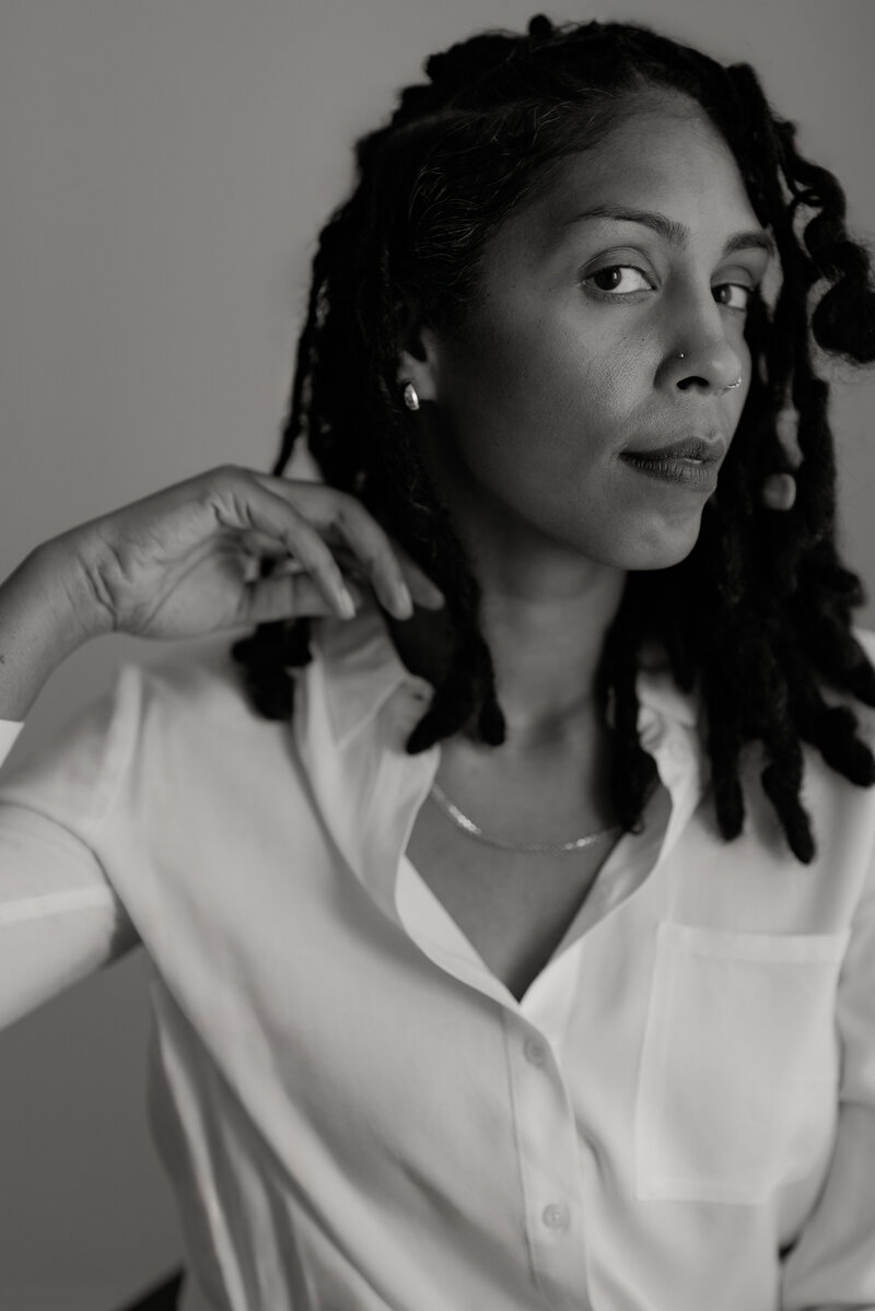 Black and white headshot of a Black woman wedding photographer based in Fort Worth, Texas. She is seated in her studio, looking directly into the camera, showcasing her professional and engaging presence