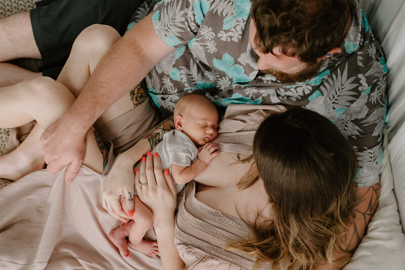 Mom in beige dress with newborn baby girl in her arms wearing gray and dad laying in a lifestyle studio in Annapolis Maryland.