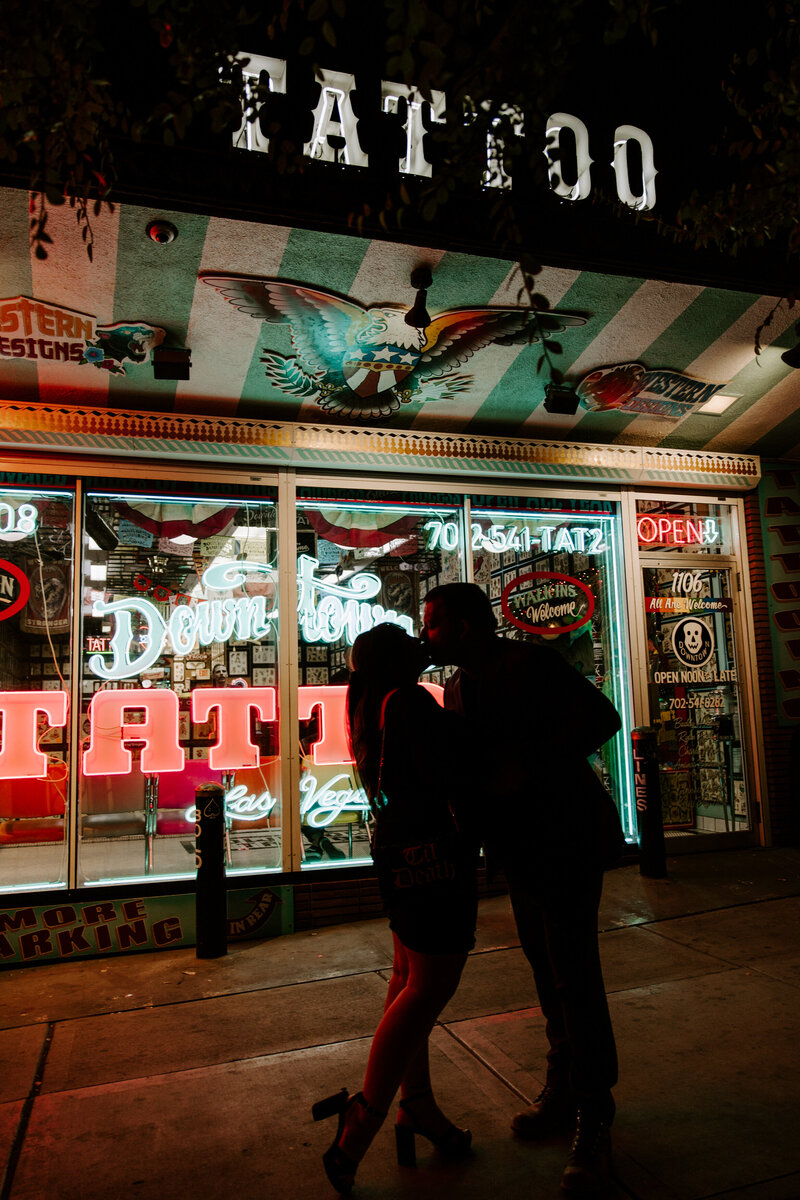 A couple kisses in front of a Las Vegas tattoo shop