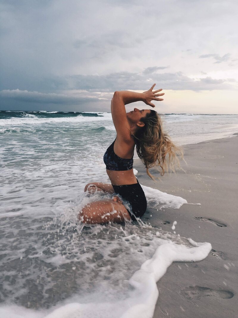 Stephanie in a yoga pose on the beach with the waves crashing on her