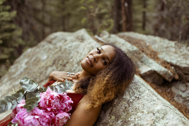 woman in a red dress leaning her back on a rock and holding a big pink flower bouquet