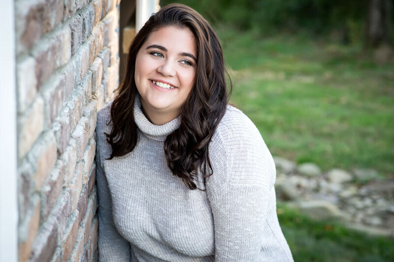 senior girl leaning on brick wall laughting