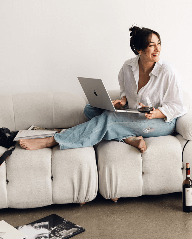 Dani Antony sitting on the couch scrolling her laptop enjoying a glass of wine in her element