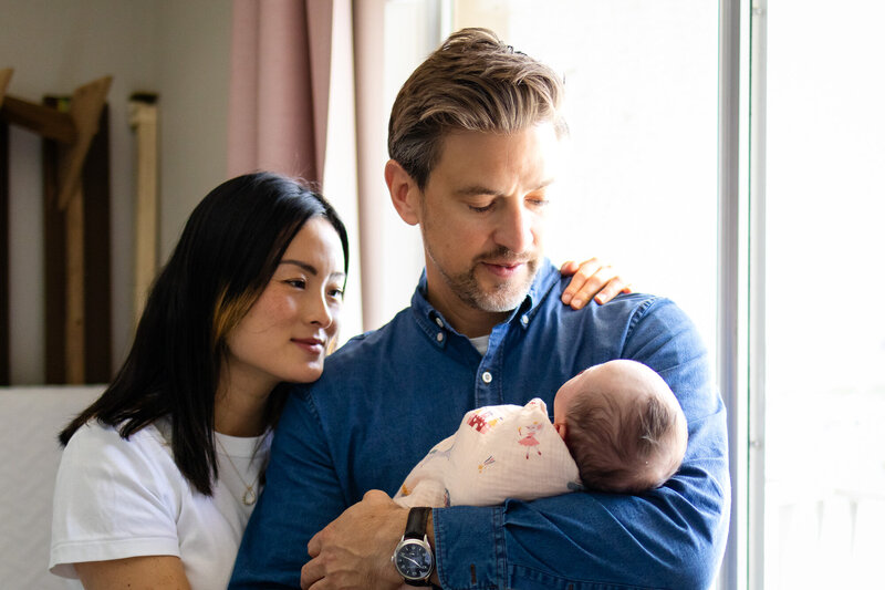 ather holding swaddled newborn as mother lovingly looks on, a warm indoor moment captured by San Francisco newborn photographer.
