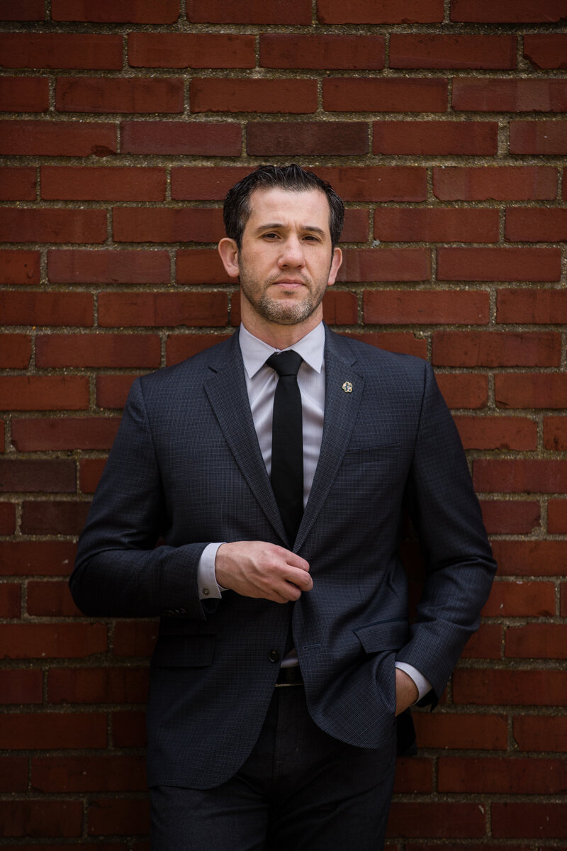 Personal branding photo of a man in a suit leaning against a red brick wall