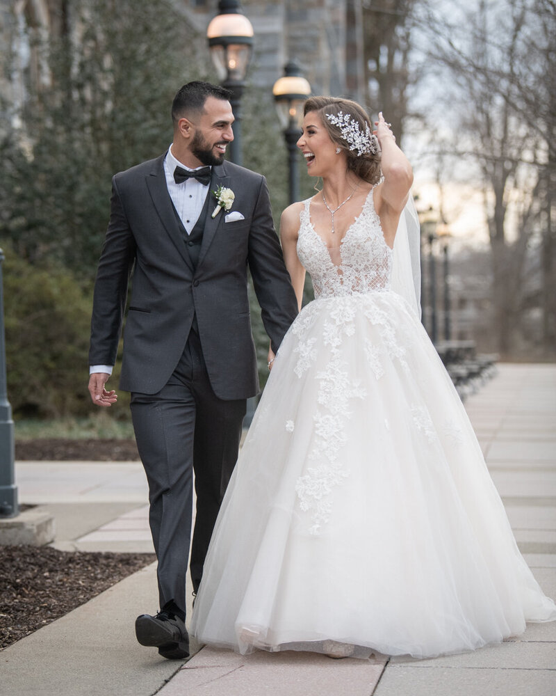 a bride and groom walk hand in hand down a sidewalk