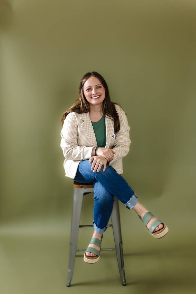 McKenna Fahrenbruch, co-founder of Graceful Exposure Media, sitting in front of a green backdrop, representing approachable and creative digital marketing for small businesses.