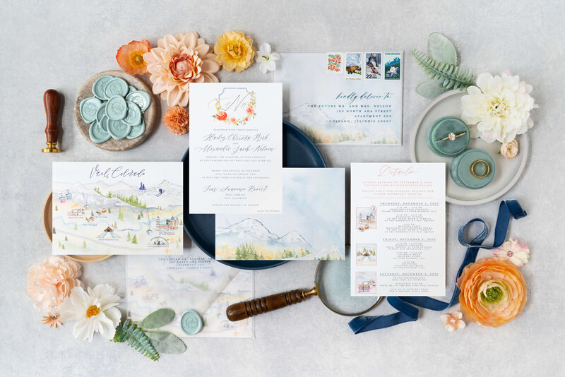 Flatlay of luxury Vail wedding invitations featuring vellum envelope, custom wax seal, watercolor map, calligraphy accents, and wedding crest
