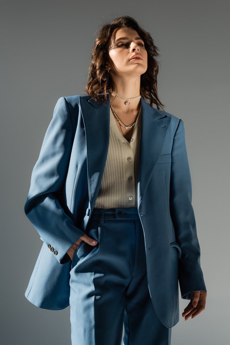 woman standing in a blue suit with one hand in pocket. 