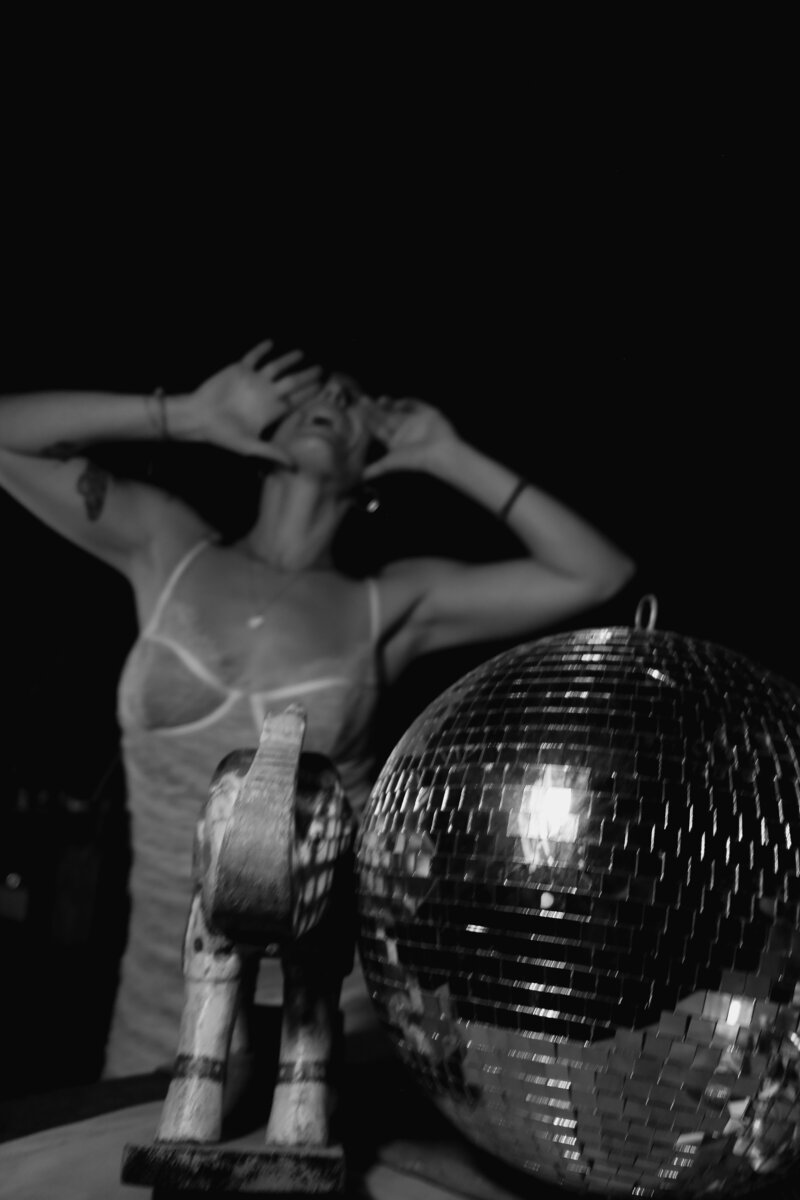Black-and-white photo of Tristan Thibodeau dancing beside a disco ball, representing bold brand expression and creative energy at Wild Woman Haus®.