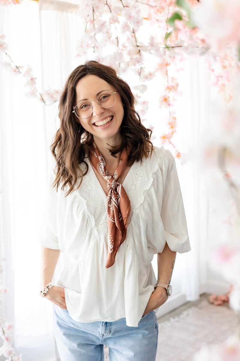 Woman smiles at camera surrounded by flowers in a studio