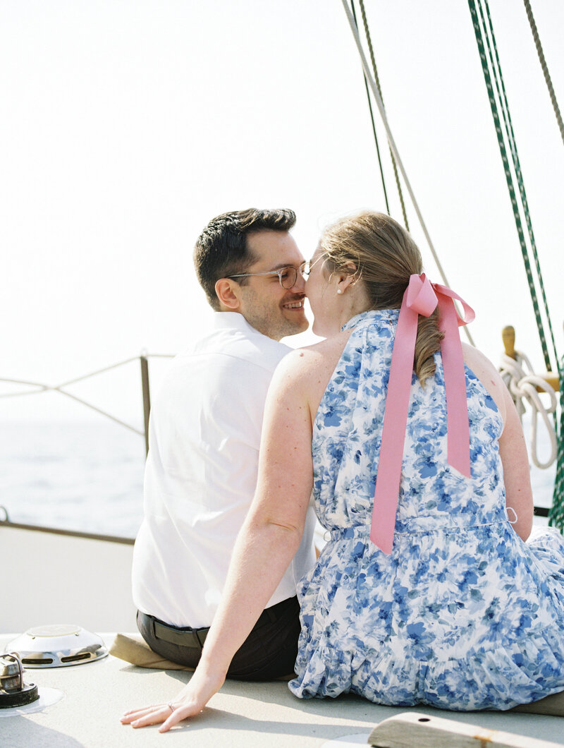 Engaged couple sharing a kiss while sitting on a sailboat during a romantic nautical engagement session, photographed by Cleveland OH engagement photographer.

