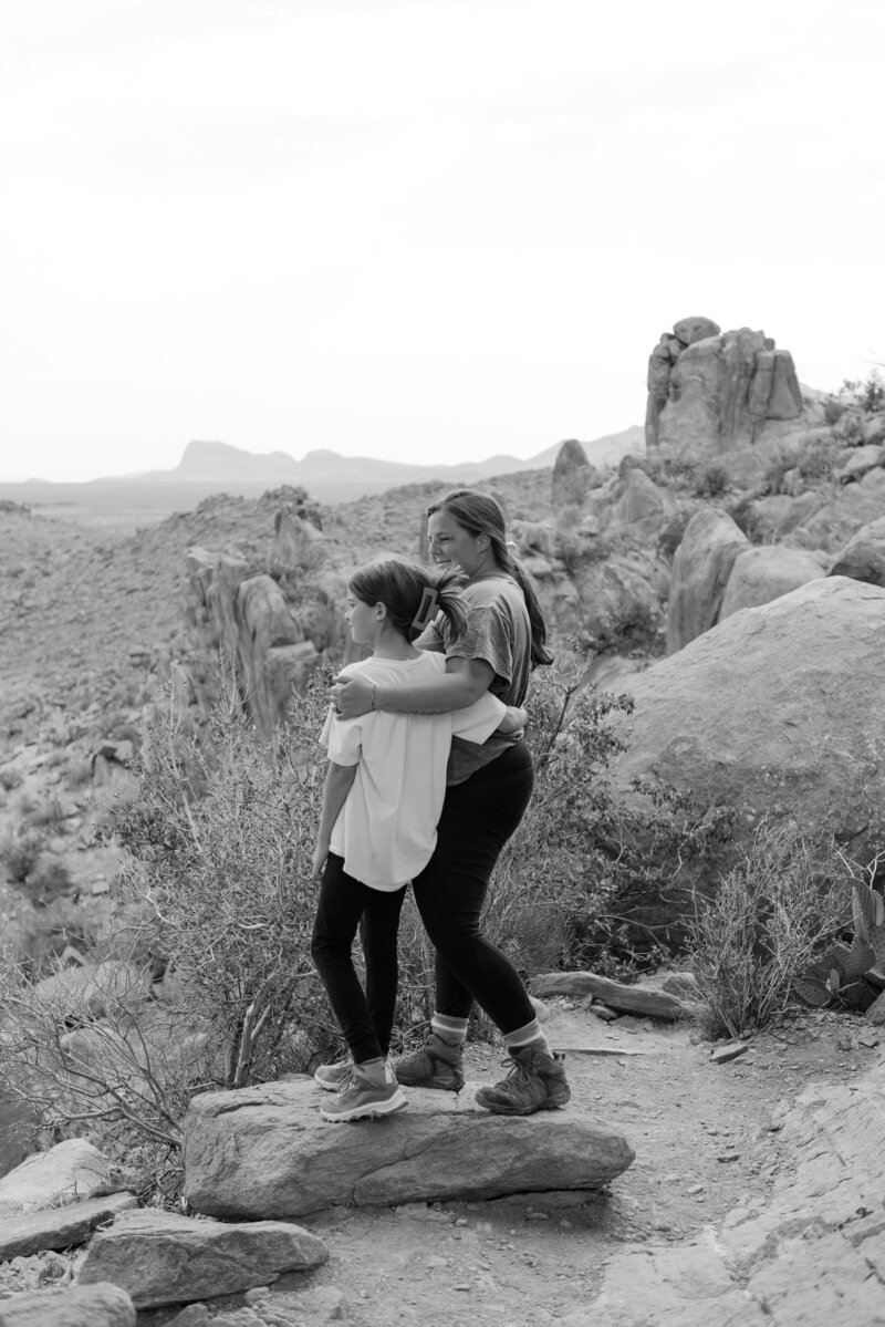 Black and white editorial-style photo of a mother embracing her daughter while overlooking the desert cliffs of Big Bend National Park. Captured by Texas wedding photographer Erin Marcin, this emotional image reflects connection, legacy, and natural light in a cinematic outdoor setting.