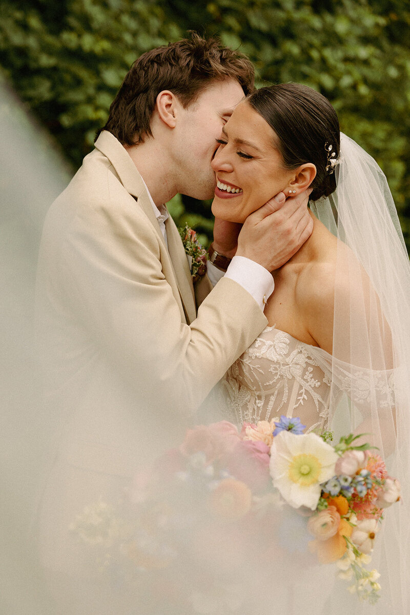 groom kissing bride on cheek and bride is holding a colourful bouquet