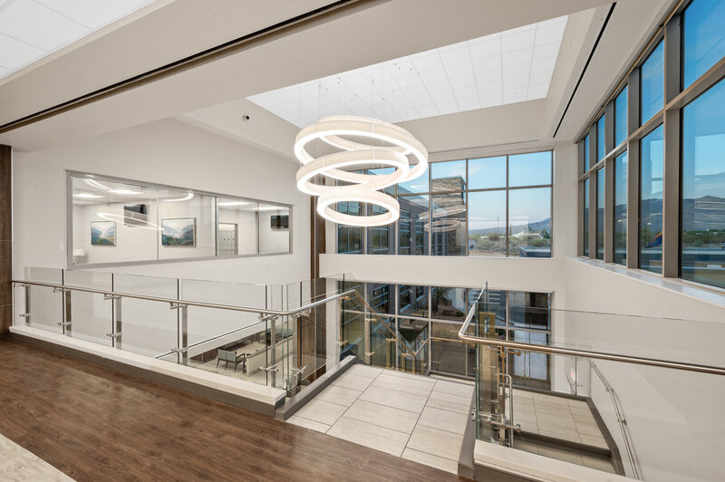 Modern office interior with large windows, circular pendant lighting, and glass railings overlooking a professional lobby space.
