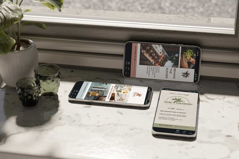 Three phones laying at different angles on a concrete counter top showing different social media posts for 'Manu Paradiso'.