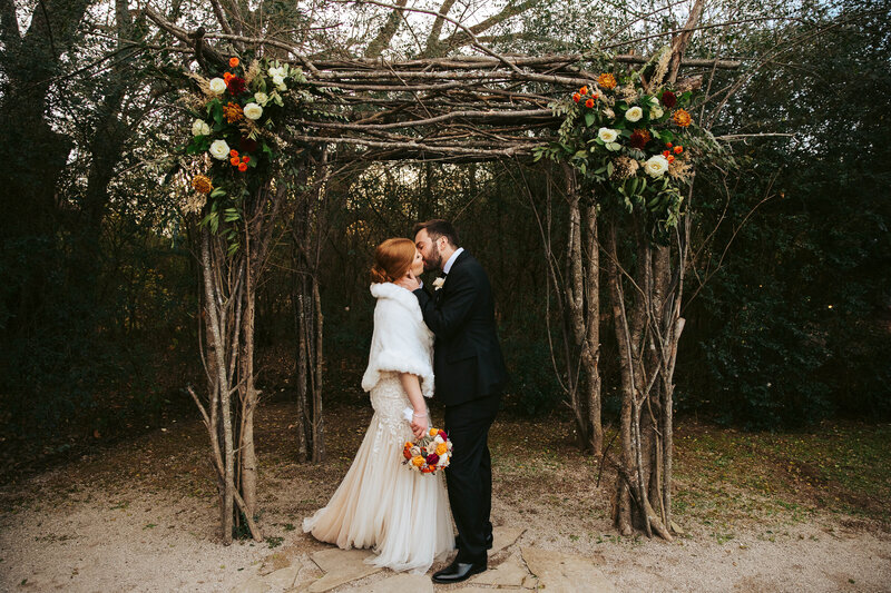 bride and groom kissing under arch with flowers