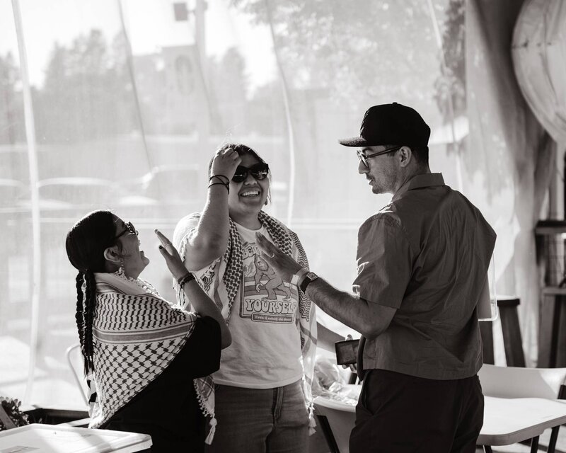Three people laughing and talking near folding table at an Asamblea BIPOC event