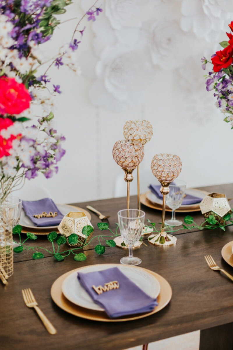 A golden glass centerpiece  with plates, utensils, and purple table napkin