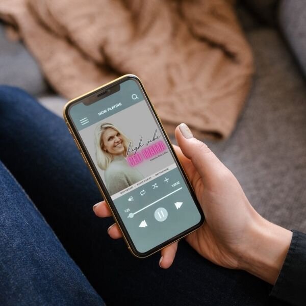 Hand holding phone playing the High Vibe CEO Mama podcast featuring Emily Collins