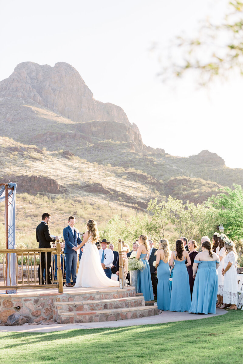 A groom and bride standing at an alter in the desert surrounded by family and friends