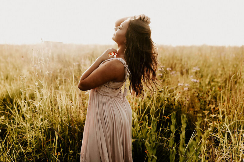 Senior girl standing in a field and holding her hair looking off in to the distance