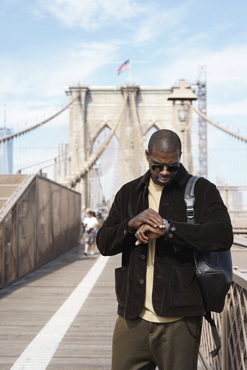 Stylish man walking alone on the Brooklyn Bridge, symbolizing personal growth and exploration through somatic therapy in Brooklyn.