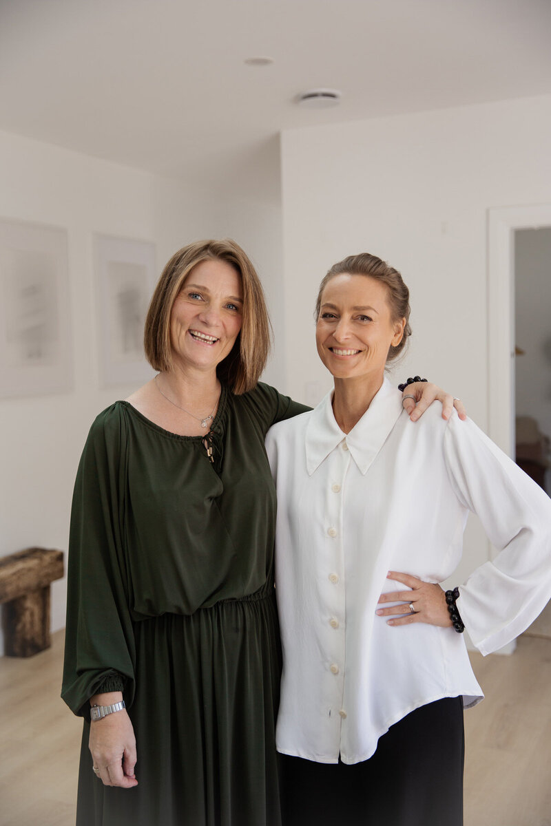 Spiritual healer Sharon Emery standing  with her arm around Naturopath Lauren Glucina in a modern home setting.