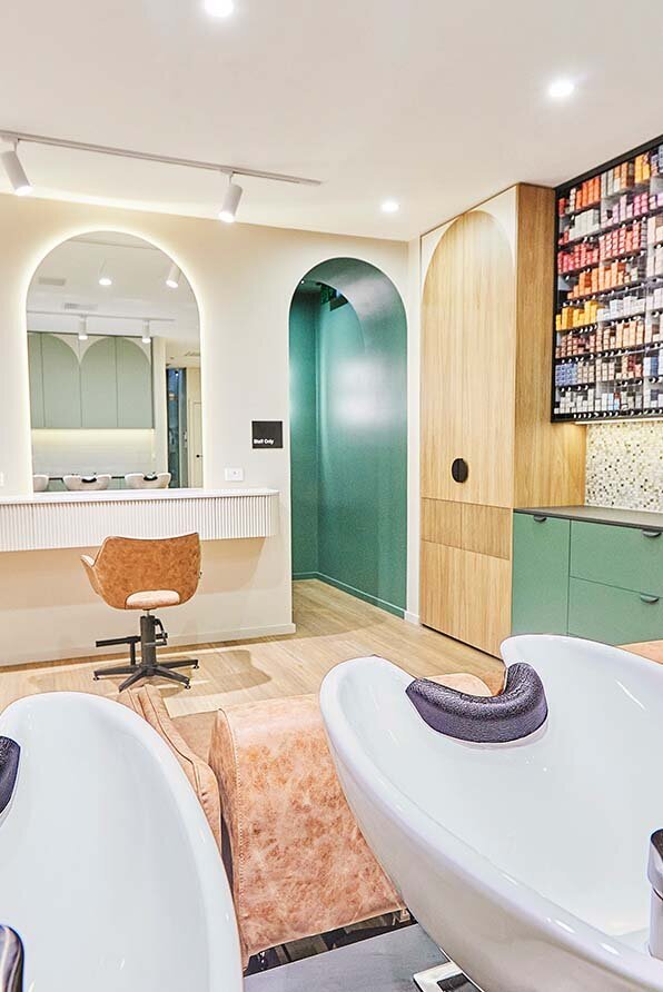 Modern salon interior featuring arched mirrors, plush beige chairs, and a vibrant display of hair products.