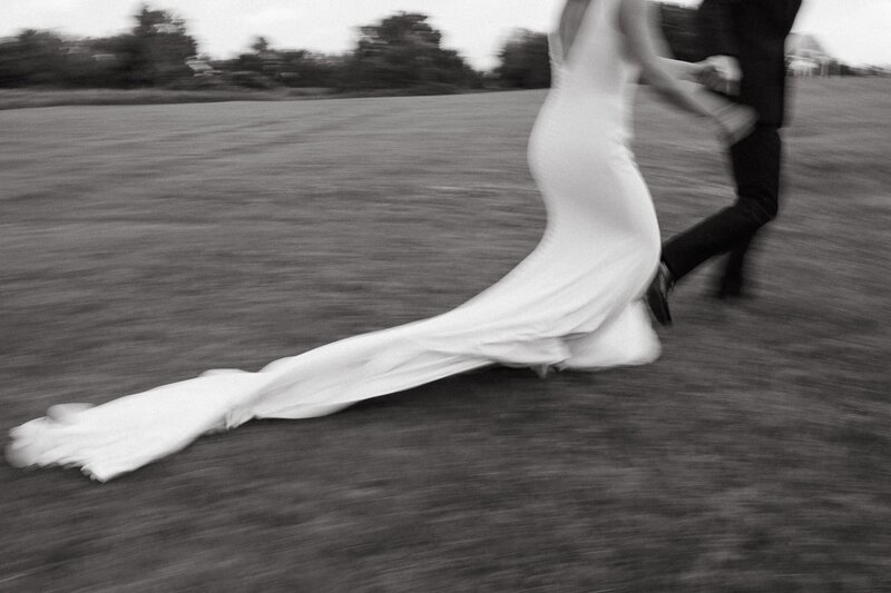 bride and groom running through a grass field