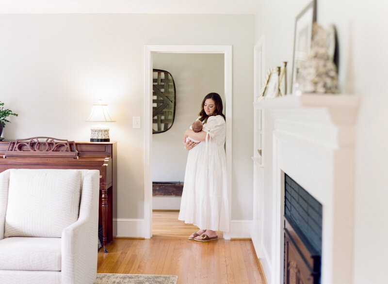 Mom sitting in front of a bright window holding her newborn daughter. Image by Raleigh newborn photographer A.J. Dunlap Photography.