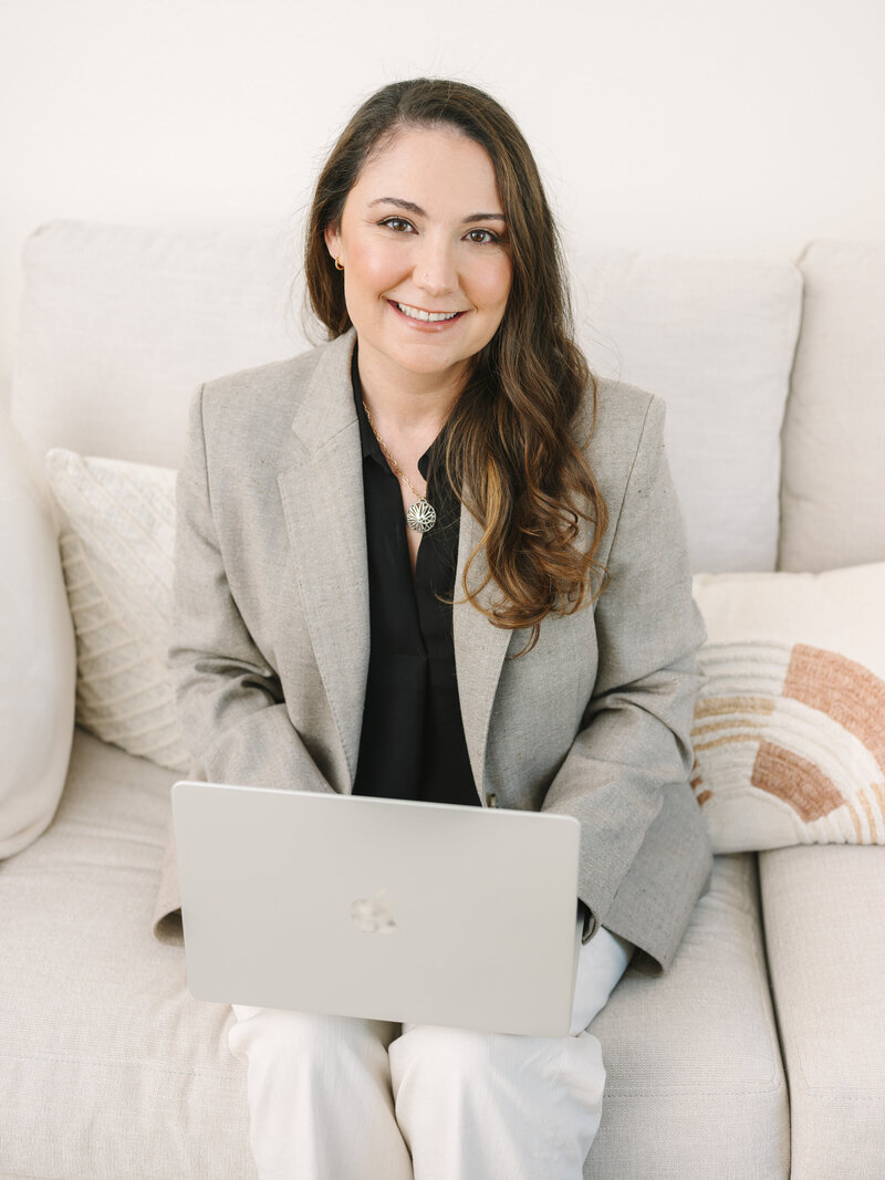 Krista Marie, a brand photographer for women, picking up her camera and smiling while working on her laptop