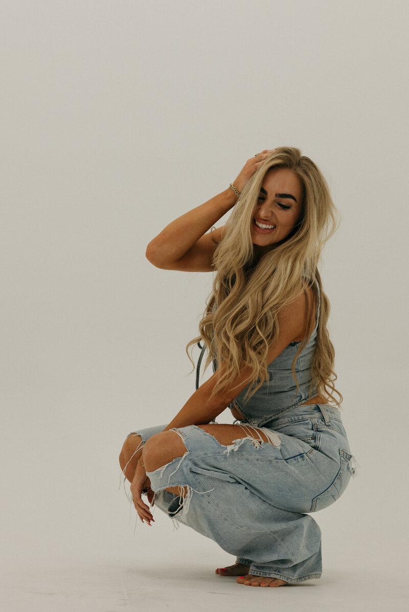 A close up of a girl holding a cowboy hat. She has a neutral face and her hand is on her neck.