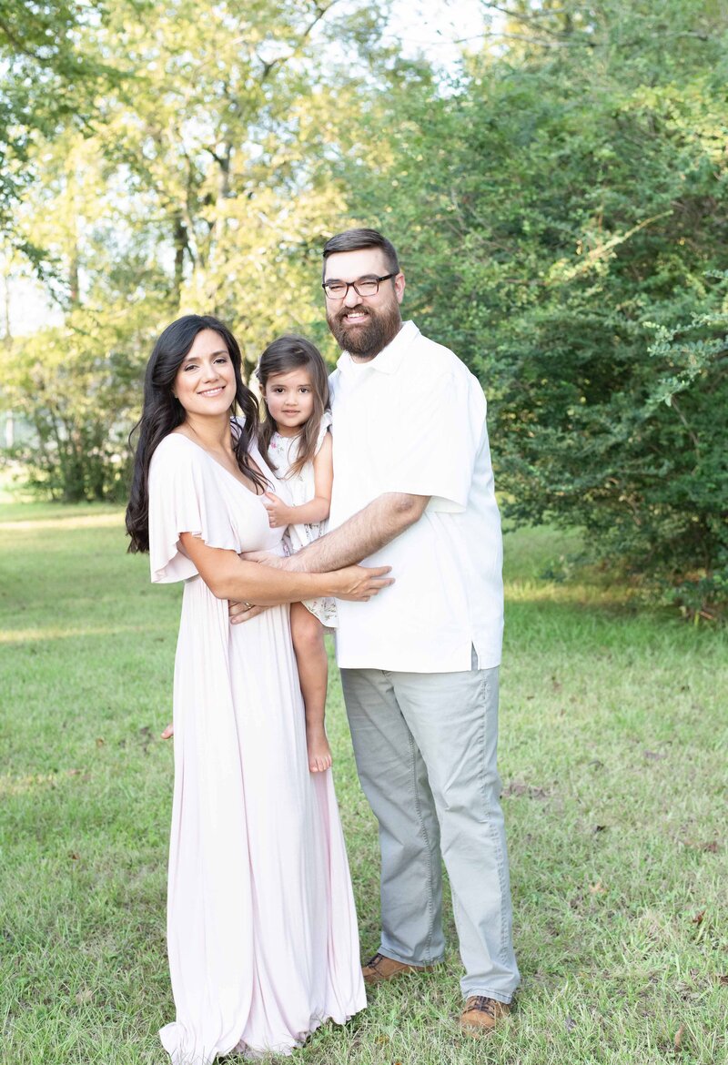 Parents embrace their daughter in a sunlit field, capturing a timeless family portrait. A heartfelt family session by Moments in Light Photography.