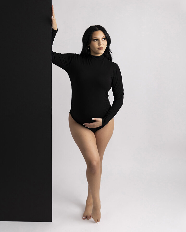 Maternity mom  to be holds belly and a black backdrop for her Greensburg maternity session.