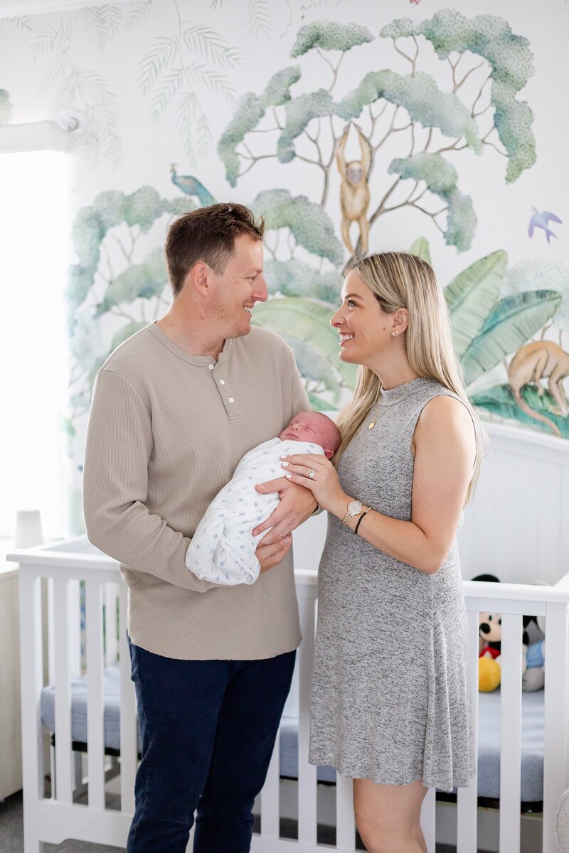parents hold baby in nursery with modern rainforest wallpaper