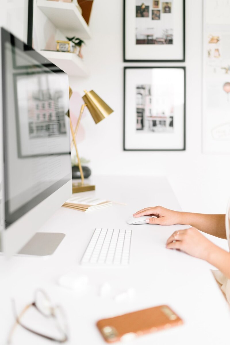 Side view of a woman’s arms working at a large Apple iMac on a modern white desk.