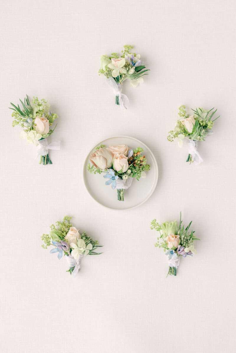 Capture the refined details of the groom and groomsmen's morning preparations with a stunning lay flat photograph of six elegant boutonnières. Perfect inspiration for sophisticated wedding day accessories.