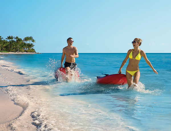 Laughing couple pulling rafts in crystal blue water at Secrets Baby Beach Aruba
