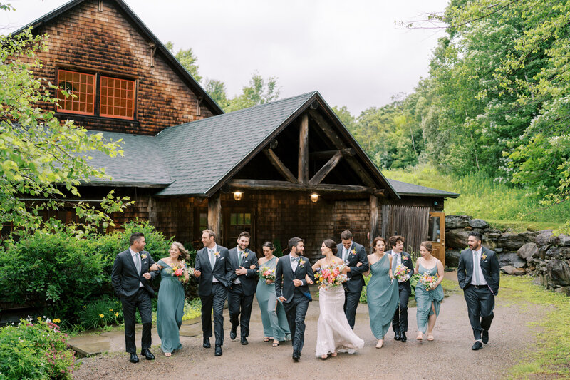 A joyful, candid moment as the wedding party walks in front of the cozy ski lodge at The Ponds at Bolton Valley in Vermont, captured in a documentary style by Jessica Leigh Photography.