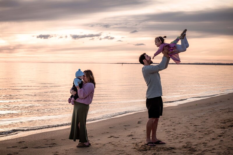 Family of four playing on the water's edge at the beach at sunset