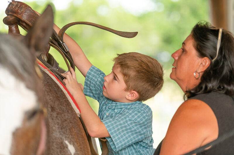 Riding instructor Lisa Laplace helps a beginner horseback student put a saddle on a paint horse