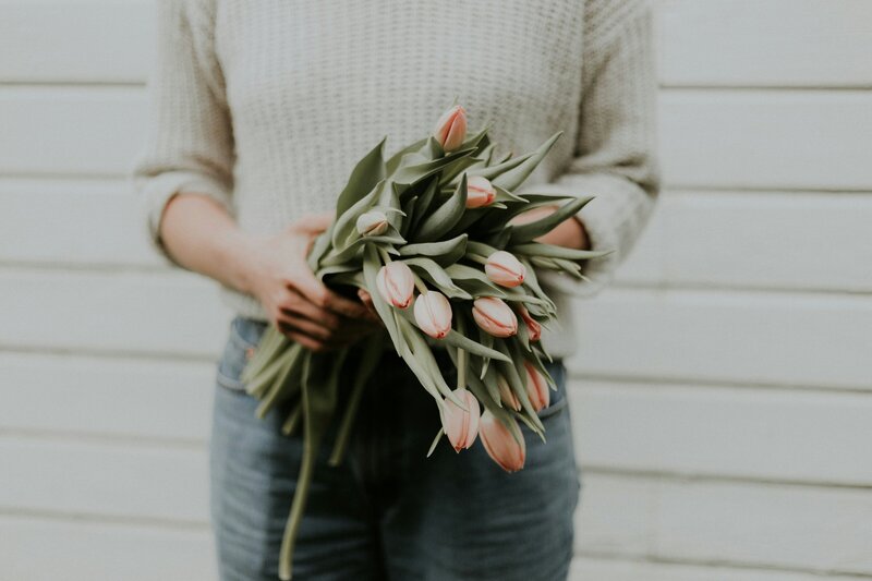 A woman with a cream jumper holds a bunch of peach tulips casually in her hands