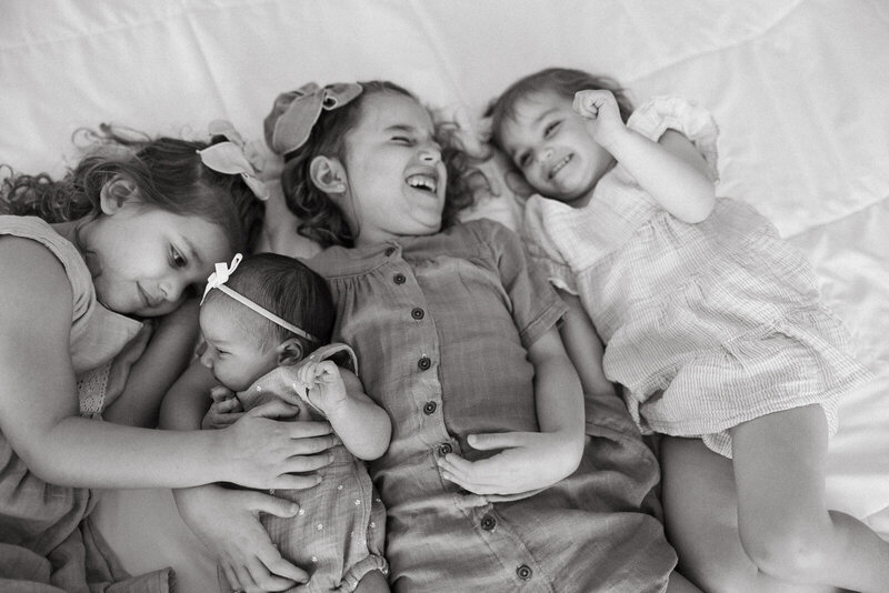 A black and white image of four sibling cuddling and laughing during a newborn session taken in Festus, Missouri. 