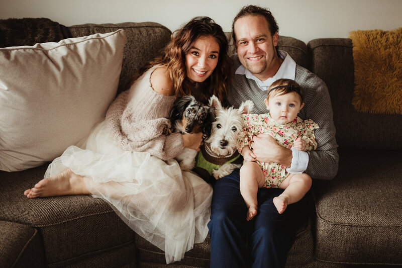 A beautiful family of three sits on the couch with their two dogs.