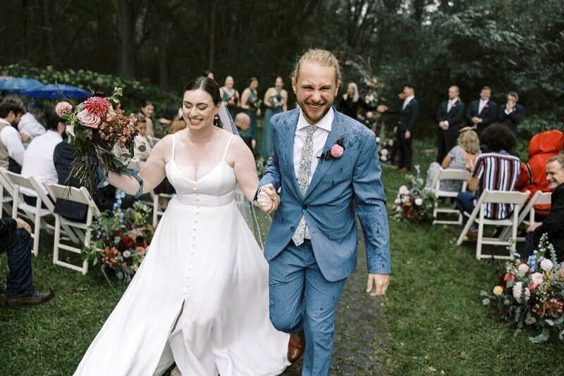 bride and groom walk down the aisle together at the end of rainy ceremony holding hands taken by st paul minnesota wedding photographer tom thornton photography